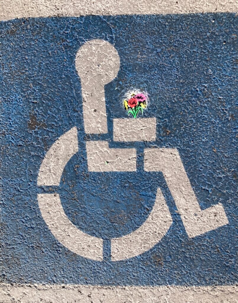 Accessibility symbol with colorful flowers added in the stick figure's hands