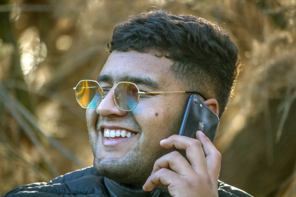 a man wearing sunglasses talking on a cell phone with a smile